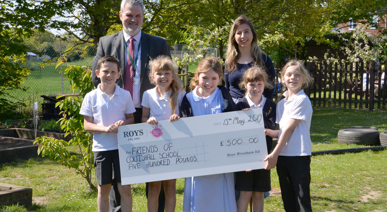 Photo of Darren Coles, Roys of Wroxham store manager presenting a cheque to Annabel Goodman and pupils from Coltishall Primary School